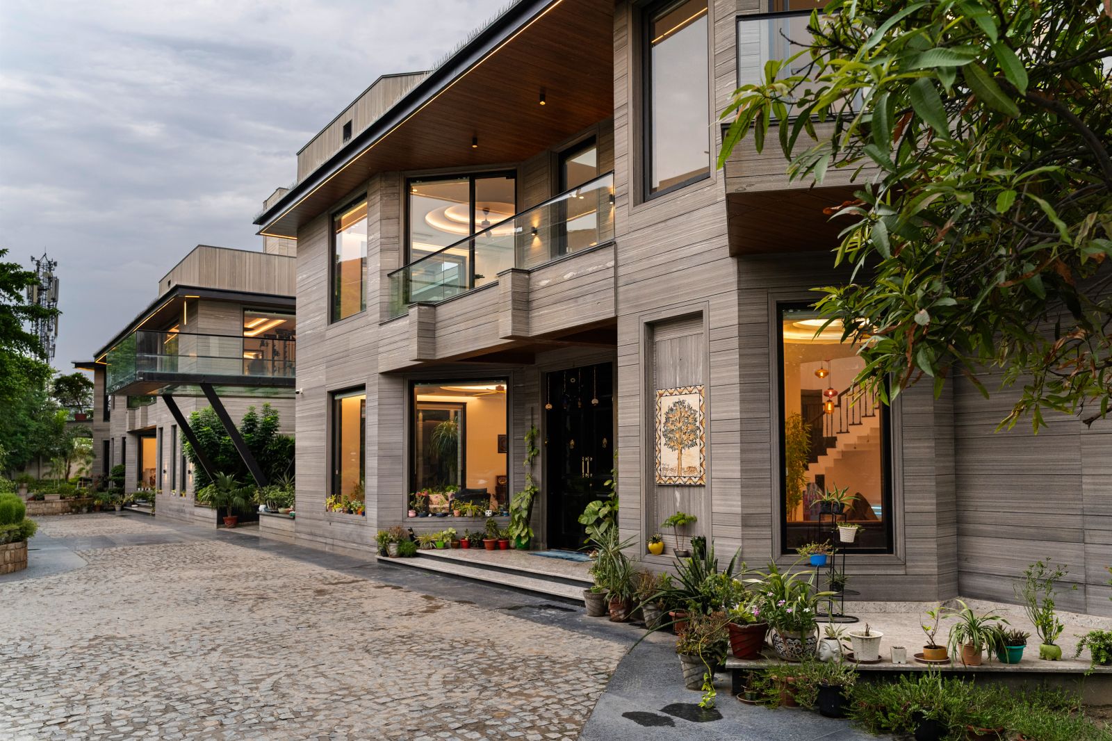 Exterior view of the Agra residence showing layered grey facade, large windows and warm interior lighting