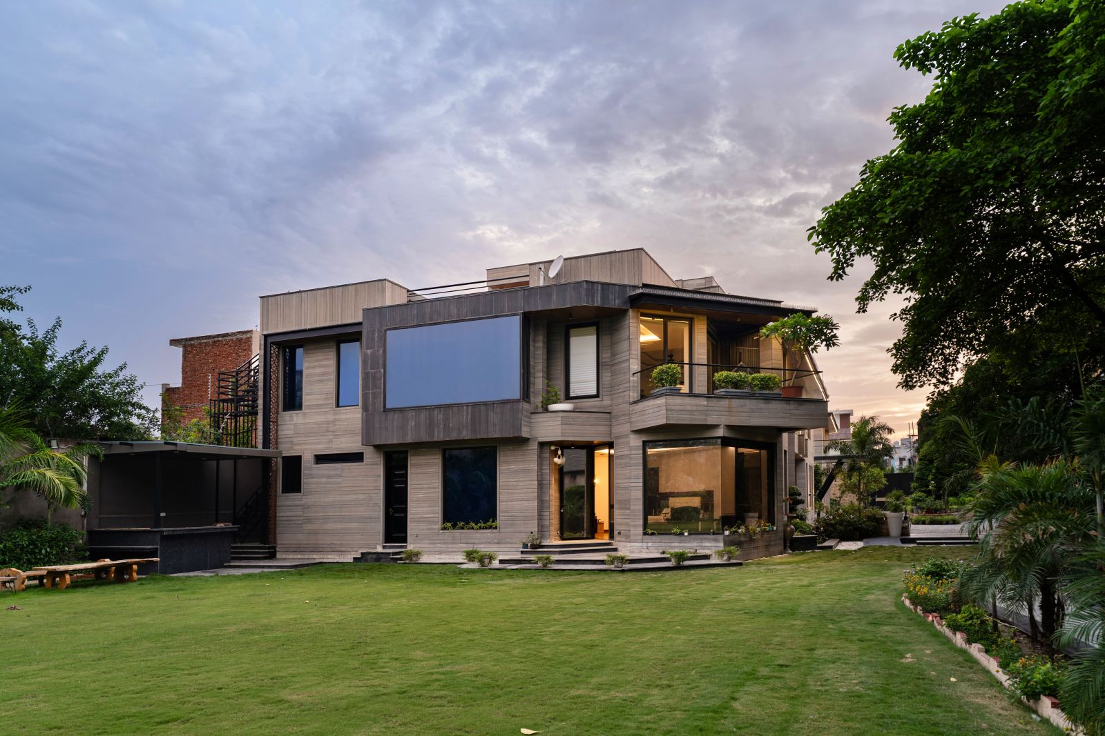 Wide view of the residence and its landscaped garden with trees, lawn and paved outdoor areas
